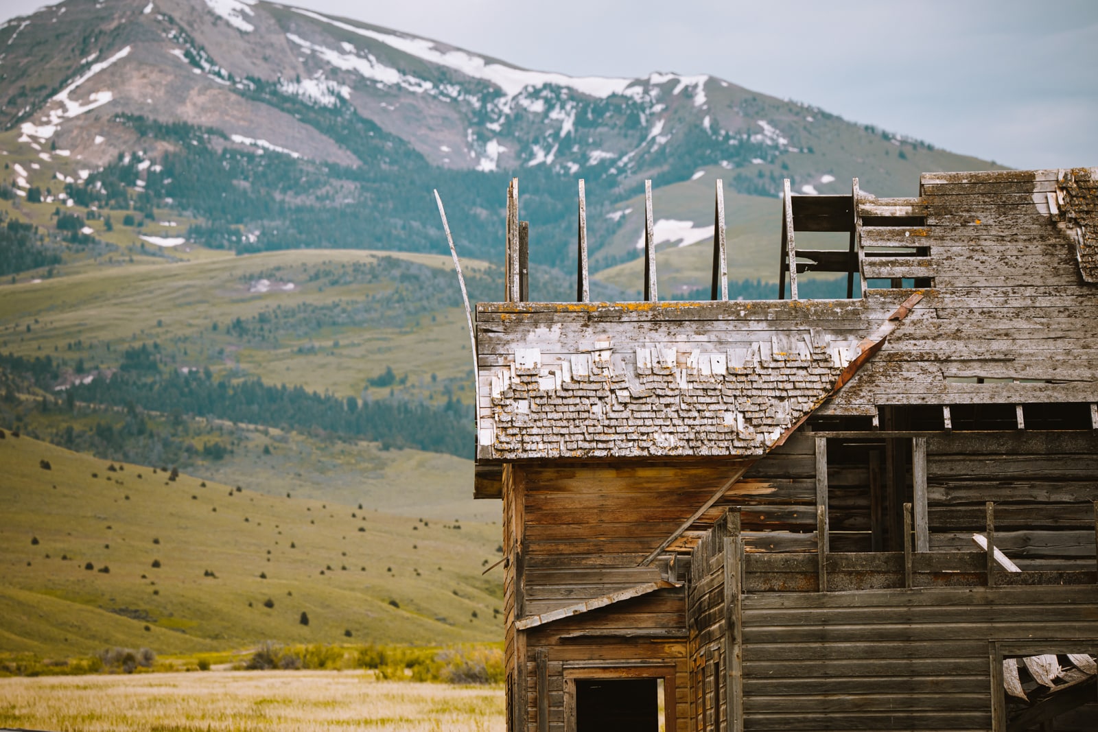An old cabin backdropped by Montana's towering mountains showcasing Upper Canyon Outfitters history tours.